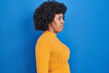 Fototapeta na wymiar Black woman with curly hair standing over blue background looking to side, relax profile pose with natural face and confident smile.