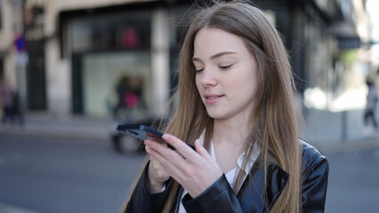 Young blonde woman using smartphone with serious expression at street