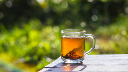 Transparent mug with fresh hot berry black tea and currant. An invigorating drink in the early morning in nature with the rays of the warm sun