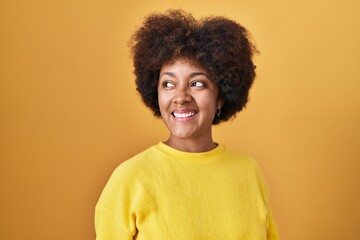 Obraz na płótnie Canvas Young african american woman standing over yellow background looking away to side with smile on face, natural expression. laughing confident.
