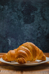 Croissants in white plate on wooden table. Side view.