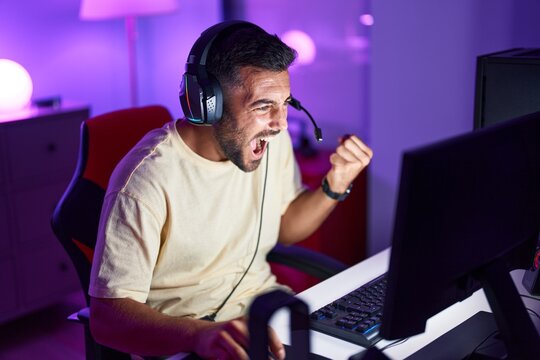 Young hispanic man streamer playing video game with winner expression at gaming room