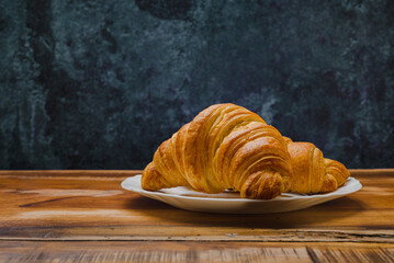 Croissants in white plate on wooden table. Side view.