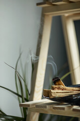 magic smoke from a burning palo santo stick lying on a natural shell incense stand on a wooden shelf in the interior Concept of mental health, selective focus
