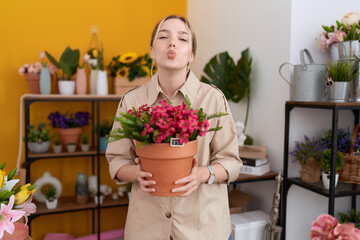 Young caucasian woman working at florist shop holding plant pot looking at the camera blowing a kiss being lovely and sexy. love expression.