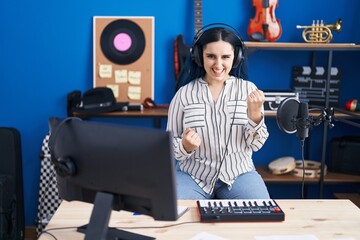 Fototapeta na wymiar Young modern girl with blue hair at music studio wearing headphones celebrating surprised and amazed for success with arms raised and eyes closed