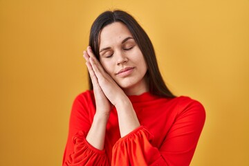 Young hispanic woman standing over yellow background sleeping tired dreaming and posing with hands together while smiling with closed eyes.