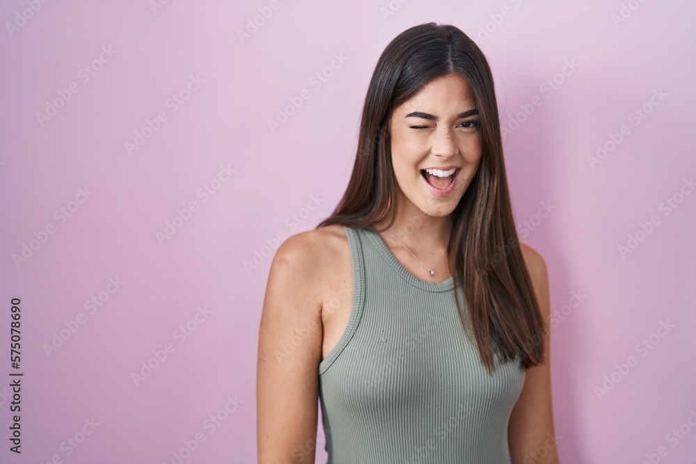 Poster hispanic woman standing over pink background winking looking at the camera with sexy expression, che