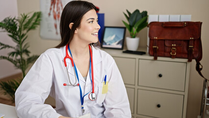 Young beautiful hispanic woman doctor smiling confident sitting on table at clinic