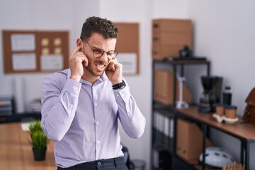 Young hispanic man at the office covering ears with fingers with annoyed expression for the noise of loud music. deaf concept.