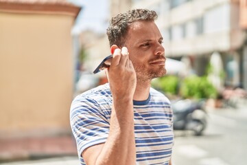 Young hispanic man listening audio message by the smartphone at street