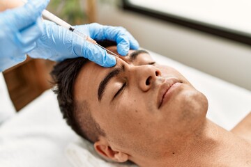 Young hispanic man relaxed having antiaging treatment at beauty center