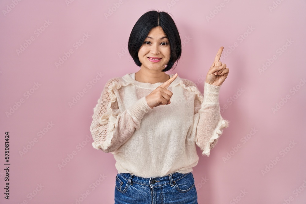 Sticker young asian woman standing over pink background smiling and looking at the camera pointing with two 