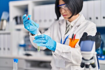 Young chinese woman scientist pouring liquid on test tube at laboratory