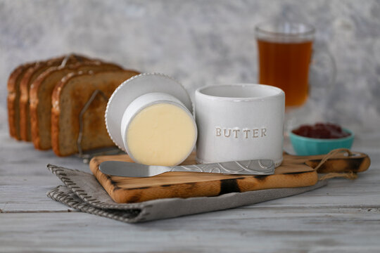 Vintage butter bell and silver knife on wood cutting board,  toast bread, tea and strawberry jam. Rustic white background.