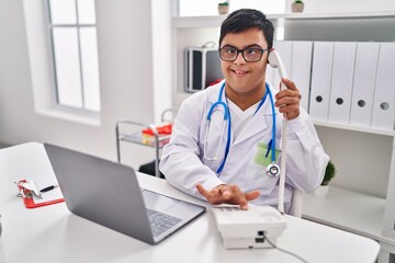 Down syndrome man wearing doctor uniform talking on the telephone at clinic