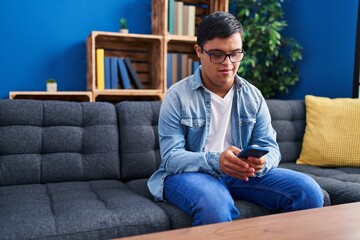 Down syndrome man using smartphone sitting on sofa at home