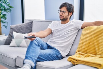 Handsome latin man holding television remote control depressed and worry for distress, crying angry and afraid. sad expression.