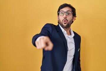 Handsome latin man standing over yellow background pointing with finger surprised ahead, open mouth amazed expression, something on the front