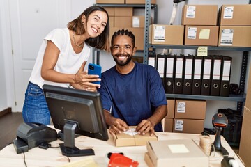 Man and woman business partners using smartphone and packing order at storehouse