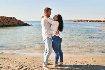 Man and woman couple smiling happy hugging each other standing at seaside