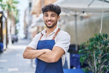 Young arab man waiter standing with arms crossed gesture at restaurant