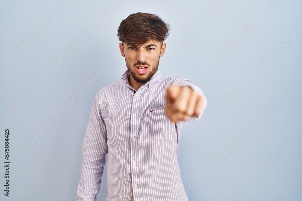 Poster arab man with beard standing over blue background pointing displeased and frustrated to the camera, 