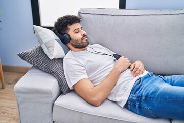 Young arab man listening to music sleeping on sofa at home