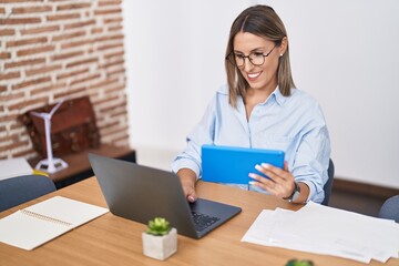 Young beautiful hispanic woman business worker using touchpad and laptop at office