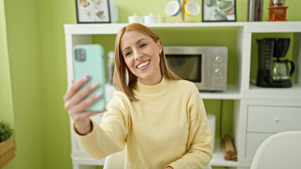 Fototapeta na wymiar Young blonde woman make selfie by smartphone sitting on the table at home