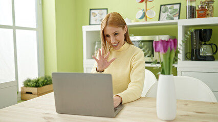 Young blonde woman having video call sitting on table at home