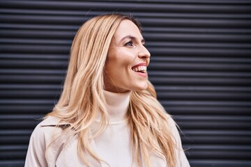 Fototapeta premium Young blonde woman smiling confident looking to the side over isolated black metal background
