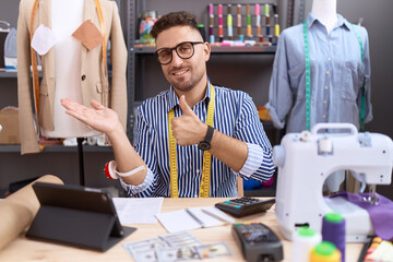 Hispanic man with beard dressmaker designer working at atelier showing palm hand and doing ok gesture with thumbs up, smiling happy and cheerful