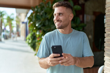 Obraz na płótnie Canvas Young hispanic man smiling confident using smartphone at street