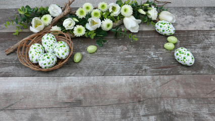 Ein Korb mit Ostereiern umrahmt von Blumen in der Farbe weiß und grün auf altem Holz Hintergrund...
