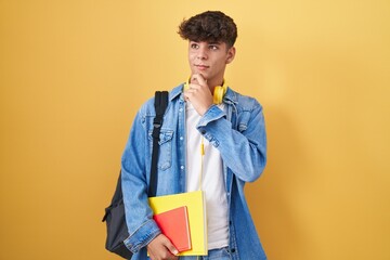 Hispanic teenager wearing student backpack and holding books thinking worried about a question,...