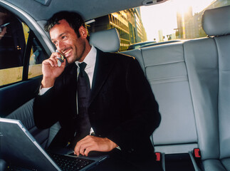 Businessman telefona e lavora al computer  seduto sul sedile posteriore di un auto