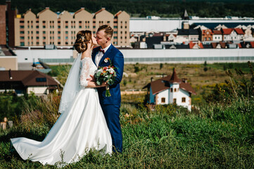 The bride and groom stand from above on a mountain on city background. Newlyweds. Wedding ceremony in country.