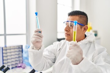 Young latin man scientist wearing covid protection uniform holding test tubes at laboratory