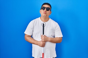 Hispanic young blind man holding cane looking at the camera blowing a kiss being lovely and sexy....