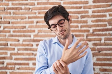 Young hispanic man standing over brick wall background suffering pain on hands and fingers, arthritis inflammation