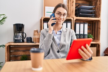 Young caucasian woman business worker talking on smartphone using touchpad at office