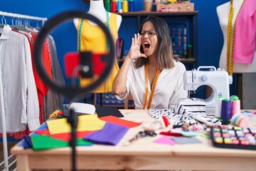 Hispanic young tailor woman recording video tutorial with smartphone clueless and confused with...