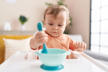 Adorable blond toddler sitting on highchair waiting to eat at home