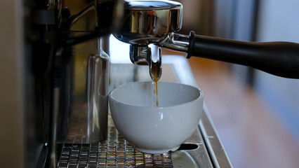 Closeup white coffee mug for hot menu, waiting for coffee brewed by coffee machine to flow into coffee cup that is waiting, from coffee handle that is plugged into coffee machine.