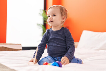 Adorable blond toddler playing with hoops toy sitting on bed at bedroom
