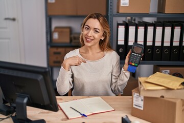 Fototapeta na wymiar Hispanic woman working at small business ecommerce holding credit card and dataphone pointing finger to one self smiling happy and proud