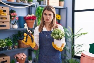 Young hispanic woman working at florist shop skeptic and nervous, frowning upset because of...