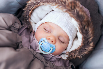 Sleeping baby with pacifier shrouded in a fur coat. Baby portrait.