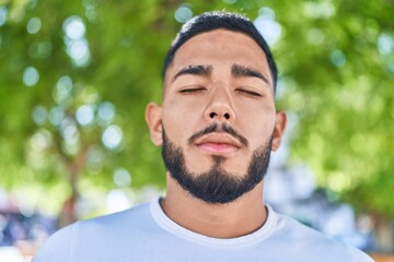 Fototapeta premium Young latin man breathing with closed eyes at park